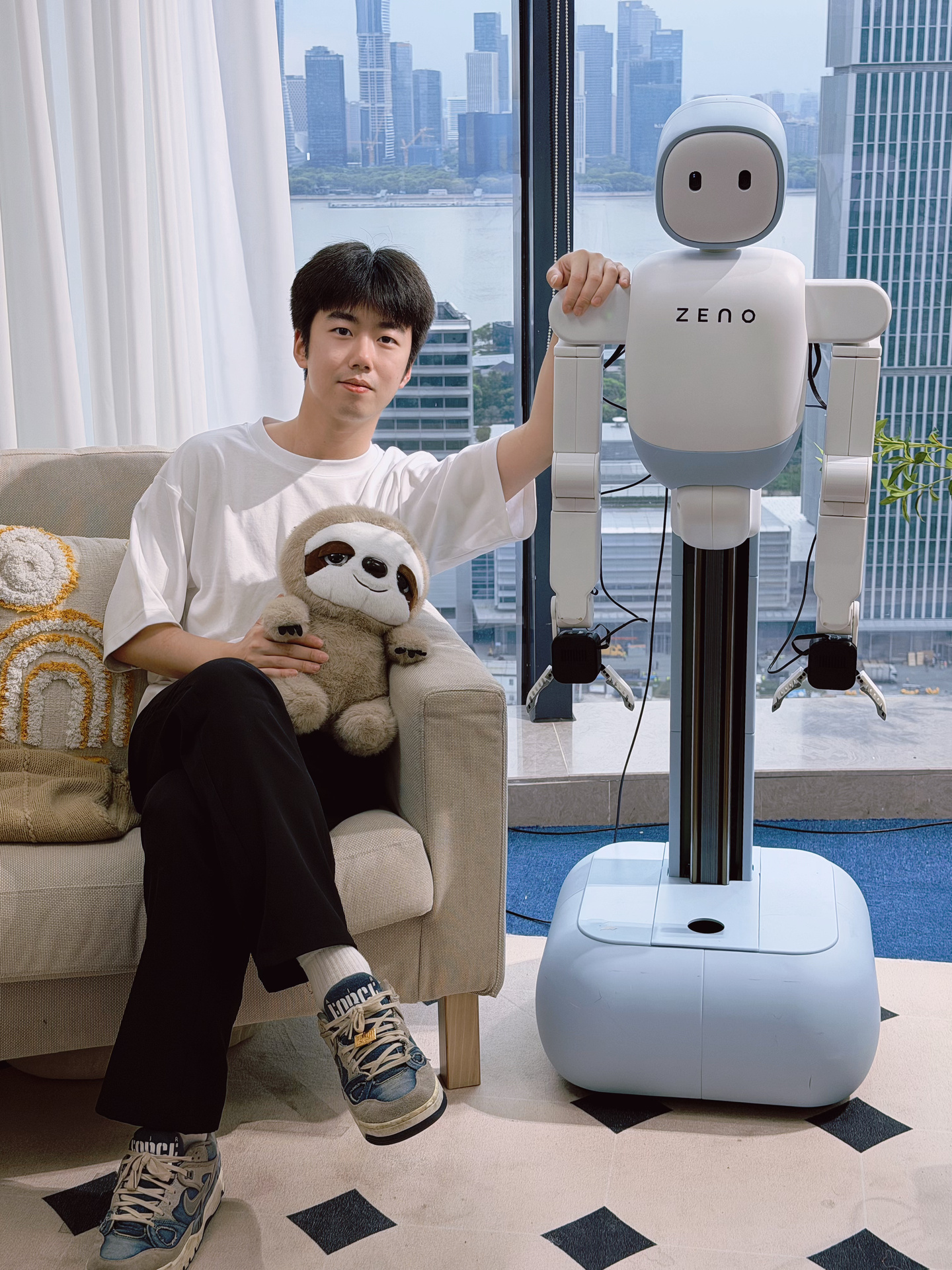Yanan Zhou seated beside a Zeno robot